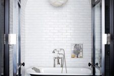 a retro black and white bathroom with white subway tiles, a black clawfoot tub, a pendant lamp and a niche for storage