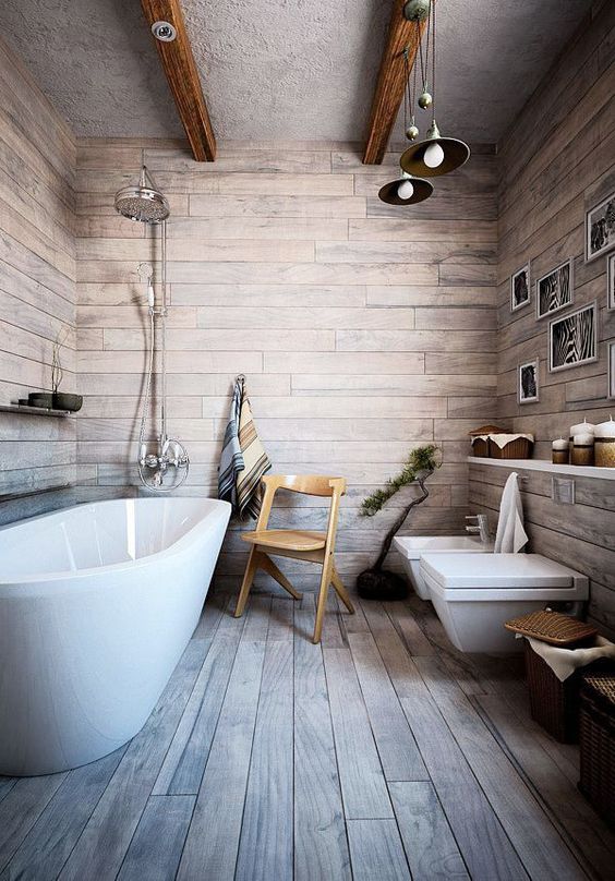 a rustic bathroom covered with weathered wood looking laminate, with wooden beams, a long open shelf and an oval tub plus pendant lamps