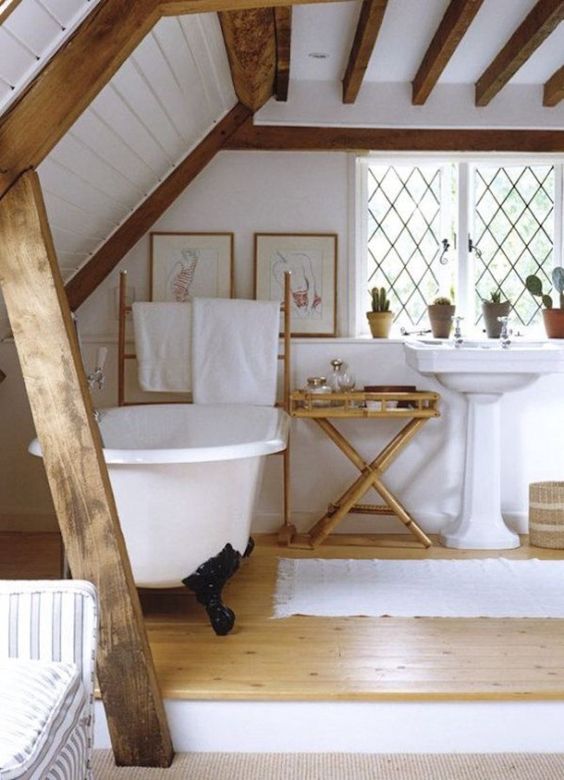 a rustic bathroom with a platform with a clawfoot tub, a free-standing sink, wooden beams, potted plants and some artworks