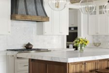 a rustic kitchen with white shaker cabinets, a stained wood kitchen island, white stone countertops, a wooden hood and pendant lamps