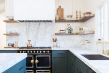 a rustic meets glam kitchen with blue cabinetry, white open shelves, a large hood and a bold black cooker