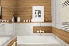 a serene minimalist bathroom clad with neutral large scale tiles and wood look ones, with a wooden vanity, some candles and an artwork