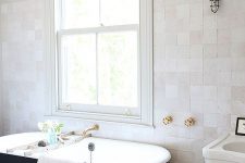 a serene neutral bathroom clad with white matte and glazed tiles, a whitewashed wooden floor, a black vintage bathtub and a floating sink