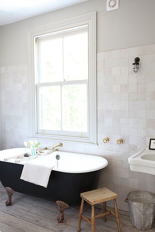 a serene neutral bathroom clad with white matte and glazed tiles, a whitewashed wooden floor, a black vintage bathtub and a floating sink