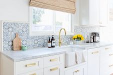 a serene white farmhouse kitchen with shaker cabinets, with white marble countertops and blue Moroccan tiles on the backsplash
