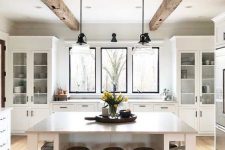 a serene white kitchen with glass cupboards and windows instead of a backsplash, a large kitchen island with open storage
