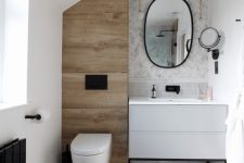 a small and chic bathroom clad with marble tiles, chevron and large scale ones, a wood look tile accent and black fixtures is stylish