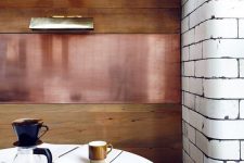 a small and cozy dining nook with a stained wood and copper wall, a round table and a built-in bench is a very cool solution