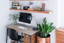 a small and cozy home office nook with open shelves, with an industrial desk, a black chair, a stool with a copper planter and lots of plants