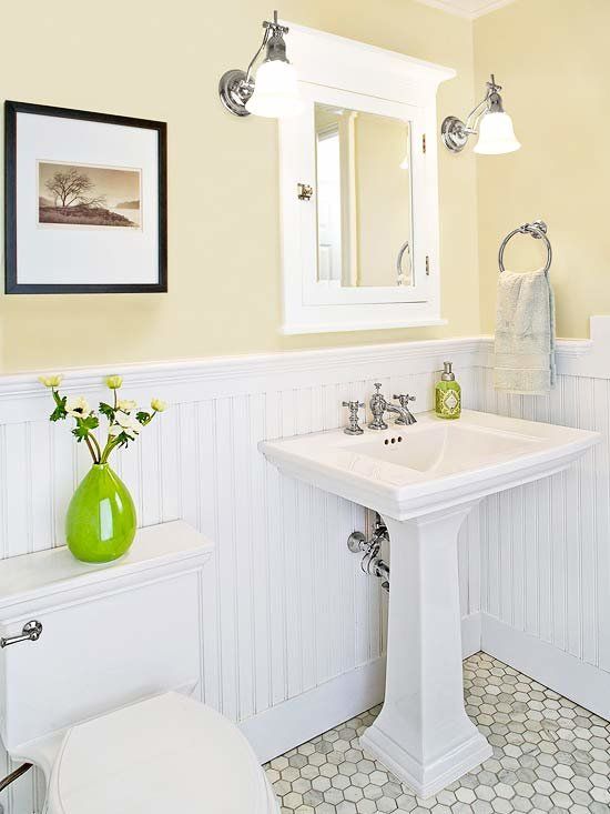 a small and cozy powder room with yellow walls and white paneling, a pedestal sink, a mirror cabinet, sconces and an artwork is very cool
