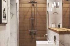 a small and refined bathroom clad with white stone tiles and with a wood tile accent in the shower, with white appliances and neutral fixtures