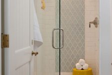a small shower space clad with white subway and blue arabesque tiles, with a niche for storage and a bold yellow stool