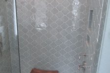 a small shower space fully clad with light grey arabesque tiles and with white penny tiles on the floor looks serene and lovely