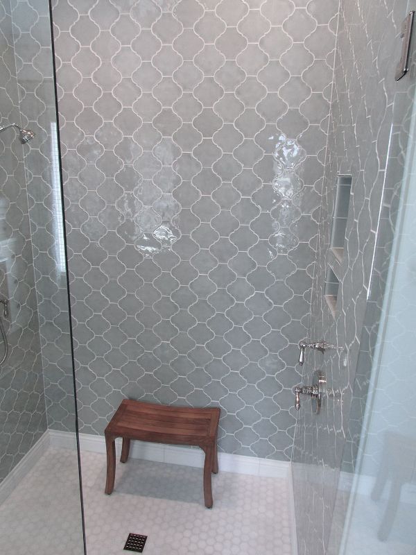 a small shower space fully clad with light grey arabesque tiles and with white penny tiles on the floor looks serene and lovely
