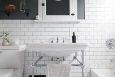 a stylish black and white bathroom clad with penny and subway tiles, with black walls, white appliannces and a console sink