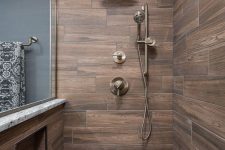 a stylish contemporary bathroom clad with wood look tiles and graphite grey ones, brass fixtures is a cool and bold idea with chic