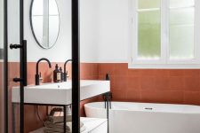 a stylish modern bathroom with white and rust-colored tiles, a console sink, an oval tub, a round mirror and a shower space enclosed in glass