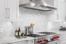 a stylish white kitchen with shaker style cabinets, grey stone countertops, a grey marble arabesque tile backsplash plus cool appliances