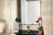 a super elegant powder room with metallic wallpaper walls, a black console sink, a mirror in a metal frame and a sconce over it