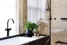 a tan stone bathroom with a shower space and a bathtub clad wiht black marble and black fixtures is a gorgeous space