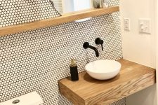 a tiny contemporary powder room clad with penny tiles, with a floating vanity and a stool, a round vessel sink and black fixtures