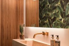 a tropical bathroom with a wood slab accent wall, a large mirror, a tropicla leaf wall, a stone floating sink and a bold pendant lamp