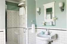 a vintage bathroom with green walls and white subway tiles, a pedestal sink, a shower space, a mirror cabinets, sconces and lamps