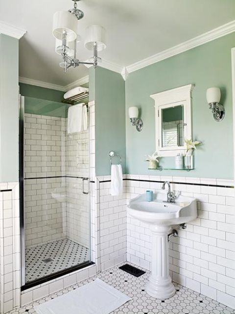a vintage bathroom with green walls and white subway tiles, a pedestal sink, a shower space, a mirror cabinets, sconces and lamps