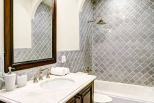 a vintage bathroom with grey arabesque tiles and mosaic ones on the floor, a stained vanity and a mirror in a stained frame