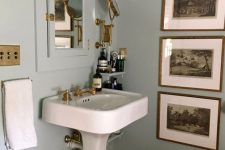 a vintage bathroom with light blue walls, a built-in storage cabinet, a pedestal sink, a vintage gallery wall, gold touches and fixtures and shelves