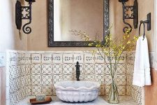 a vintage bathroom with tan and peachy walls, pretty patterned tiles, a shabby chic vanity with a refined stone vessel sink and vintage sconces