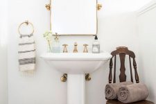 a vintage bathroom with terracotta tiles on the floor, a vintage pedestal sink, a mirror in a gilded frame, sconces and a basket for storage