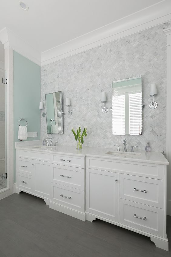 a vintage neutral bathroom with a mint green accent wall, a white marble arabesque tile wall, white vanities and sconces and mirrors