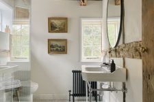 a vintage neutral bathroom with a wooden ceiling and beams, hex tiles, a free-standing sink, a mini gallery wall and a round mirror