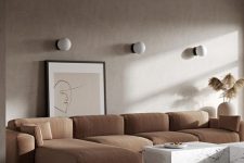 a warm-toned neutral living room with taupe walls, a rust-colored sectional, white marble coffee tables and wall lamps