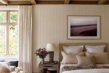 a welcoming bedroom with wooden beams, a tan bed, stained nightstands, a navy sofa and neutral bedding and textiles