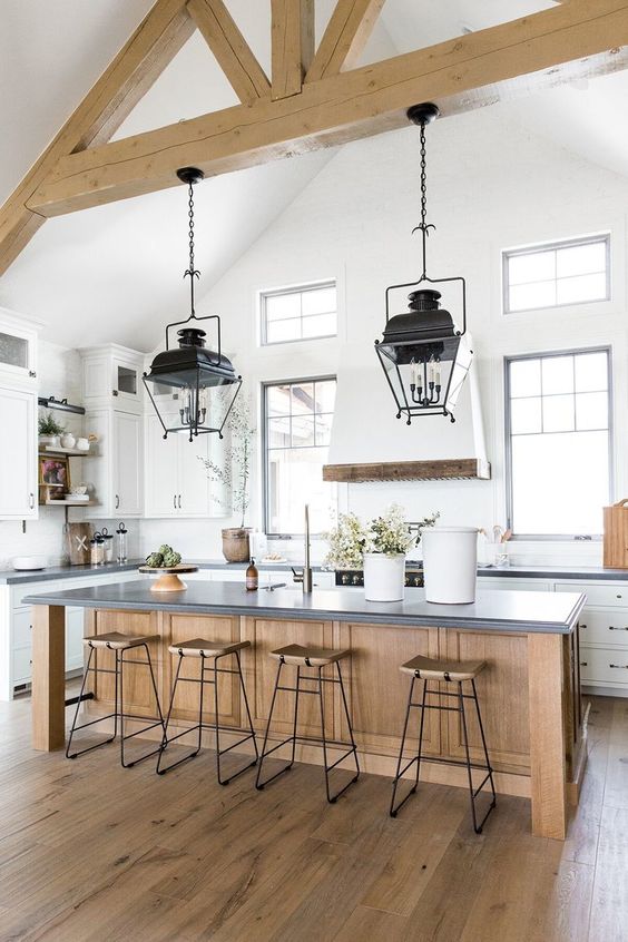 a white and airy famrhouse kitchen with a stained kitchen island, wooden stools, wooden beams and black pendant lamps