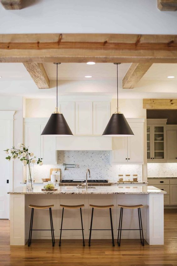 a white and grey kitchen with a large kitchen island, white stone countertops, light stained wooden beams and black pendant lamps