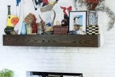 a white brick built-in fireplace with a wood slab mantel, with lots of books inside and candles and various art on the mantel is a stylish idea