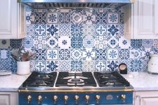 a white cottage kitchen with shaker cabinets, a bold blue cooker and a matching hood, bright blue Moroccan tiles on the backsplash