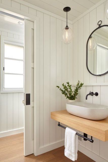 a white farmhouse bathroom with planked walls, a floating vanity and a rounded vessel sink for a chic look and black touches