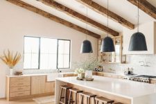 a white farmhouse kitchen with stained cabinets, a stained kitchen island and stools and stained wooden beams