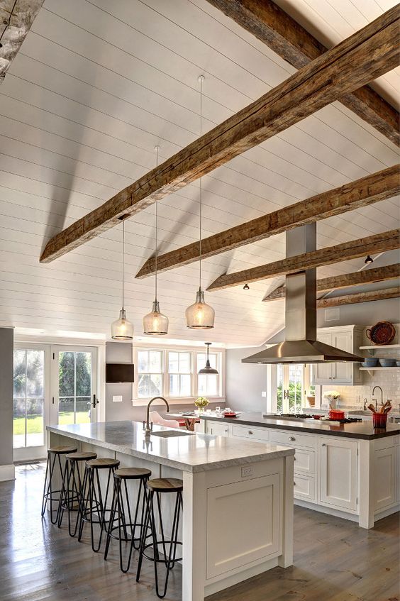 a white farmhouse kitchen with weathered wooden beams, white shaker cabients and a large kitchen island, an additional one with an eating zone
