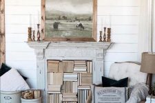 a white farmhouse space with planked walls, refined furniture, buckets with firewood and a shabby chic fireplace used for storing books