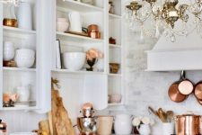 a white glam kitchen with open shelves, with elegant crystal chandeliers and copper cookware and tableware for a soft warm touch