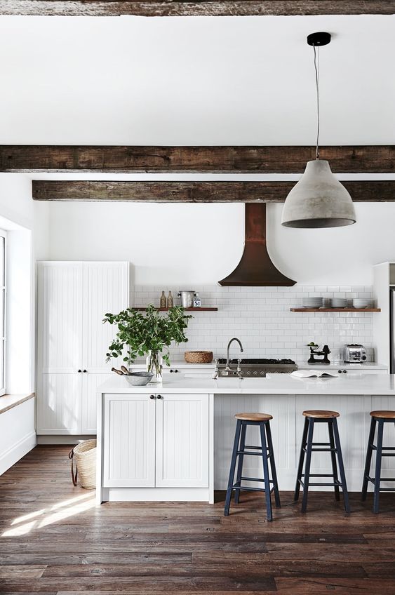 a white kitchen with planked cabinets, a large kitchen island, a white subway tile backsplash, dark wooden beams and a concrete pendant lamp