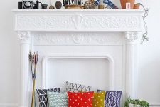 a white non-working fireplace with a refined mantel, with colorful pillows and arrow inside it, with some decor on the mantel
