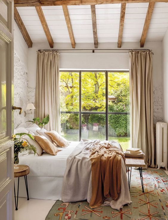 an English countryhouse bedroom with wooden beams, a bed, wooden stools and a bench on hairpin legs and mustard bedding