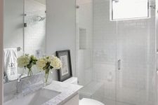 an airy white bathroom clad with white subway, penny tiles and grey arabesque tiles to accent the floor, a white vanity with a stone countertop
