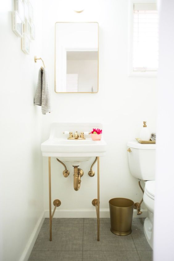 an all white powder room with a console sink, a brass trash bin, a mirror in a brass frame and a mini gallery wall